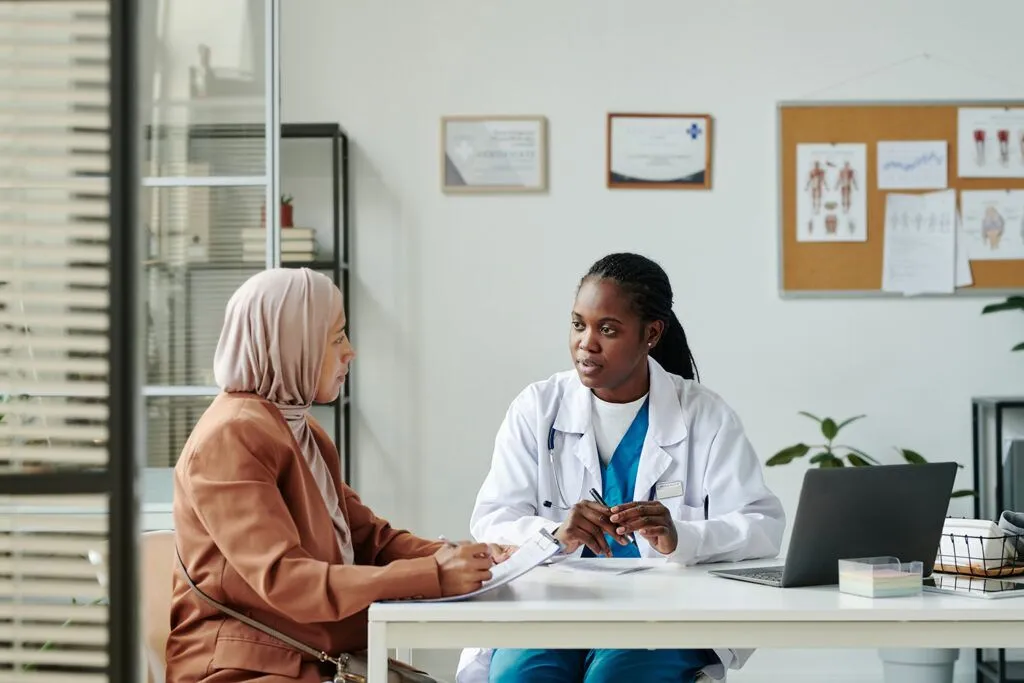 Young African-American female clinician in lab coat talking to a patient.
